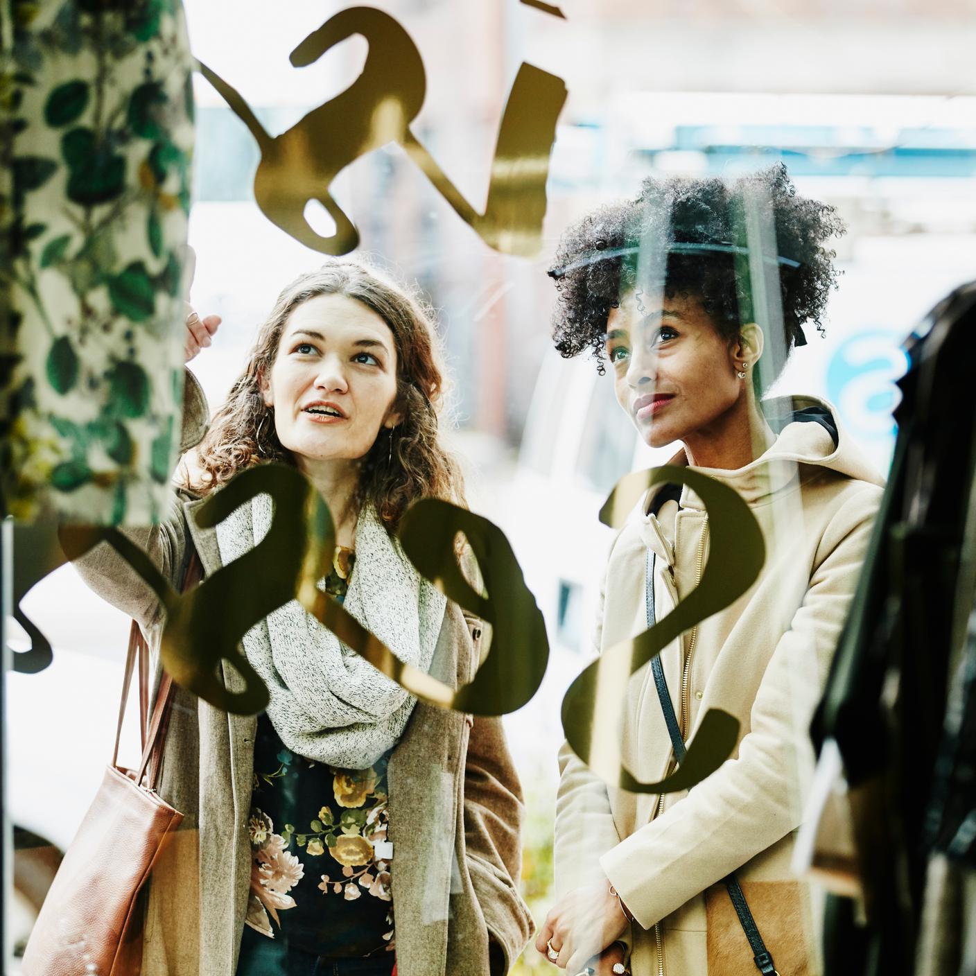 Woman showing friend dress in window of boutique