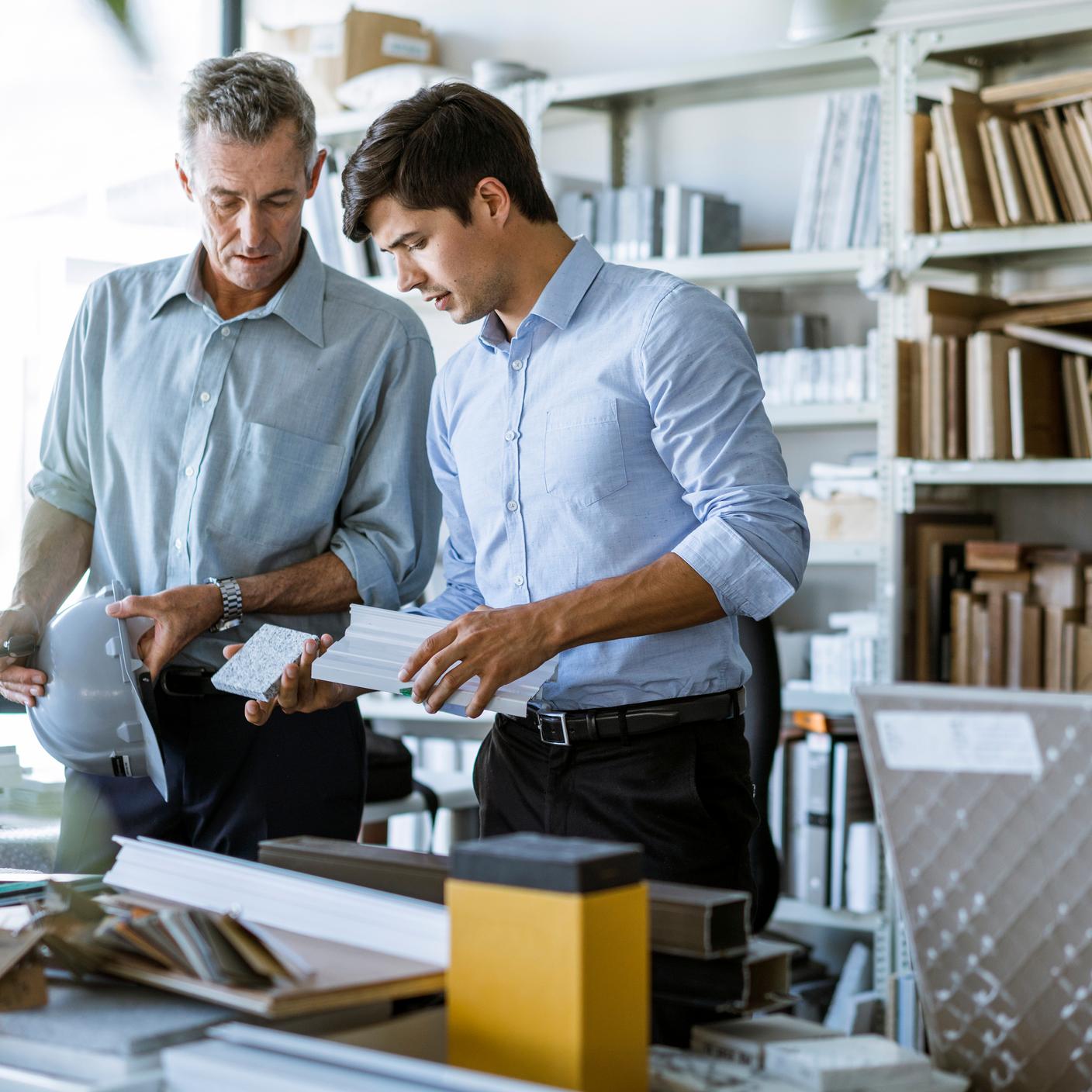 Gebäude und Bauwesen - Architekten mit Bauausrüstung am Schreibtisch im Büro