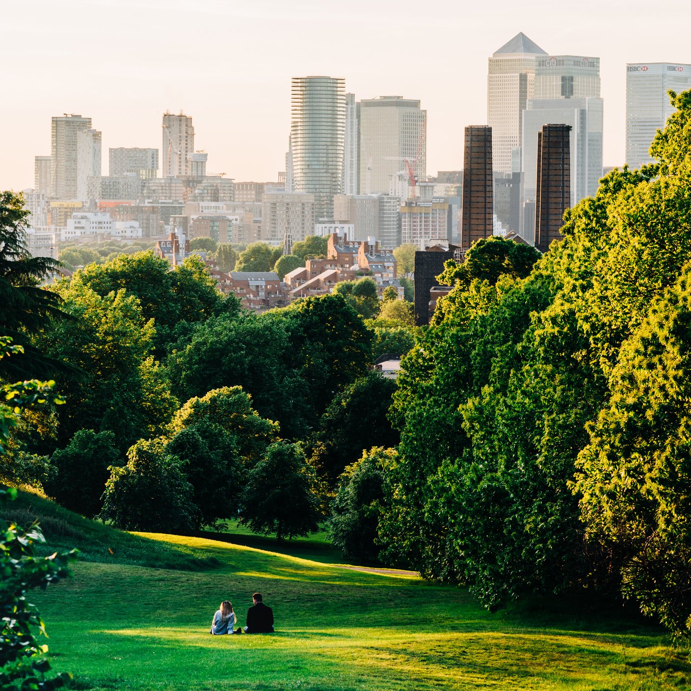 A couple sit in Greenwich Park, London looking the Canary Wharf skyline