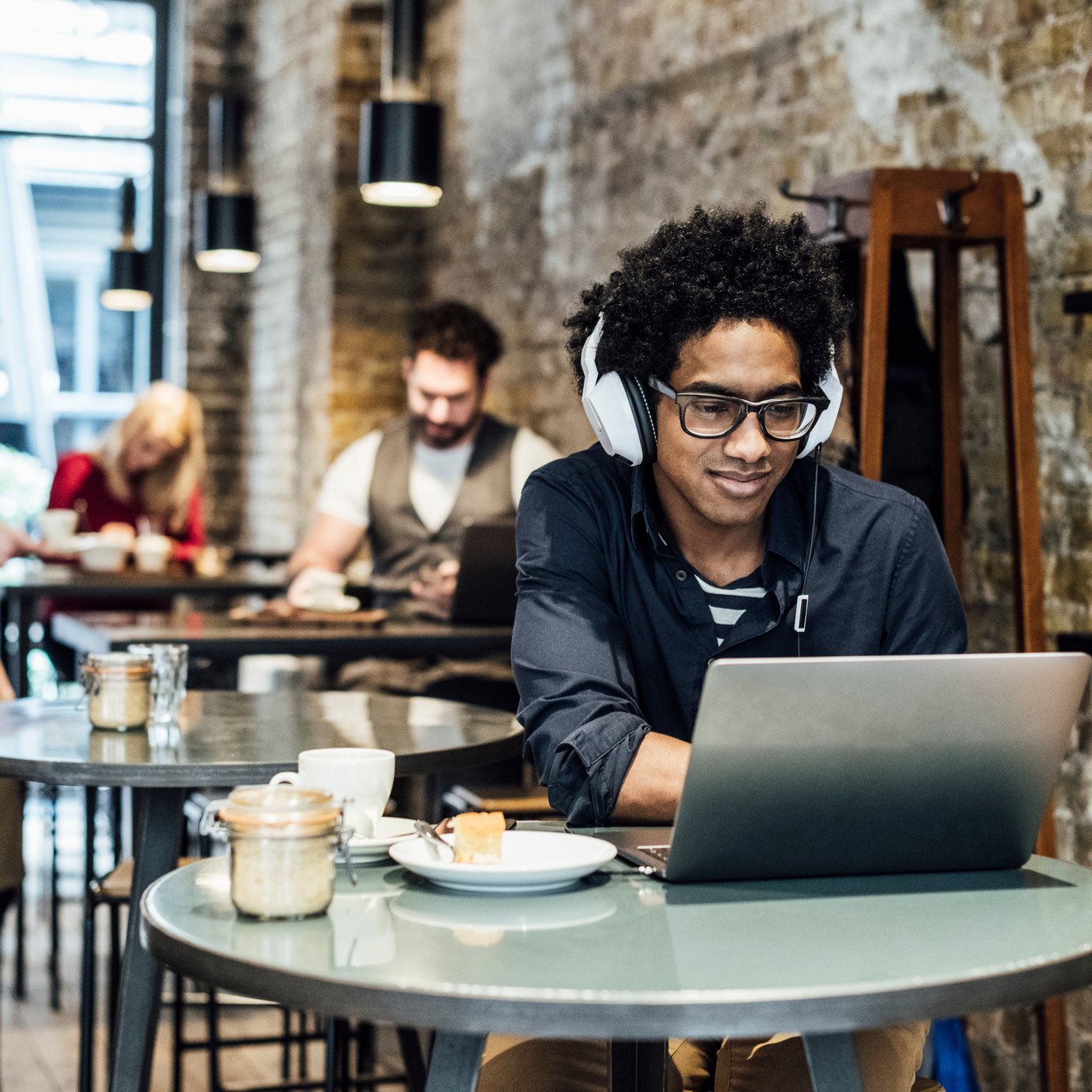 Male customer sitting at table wearing headphones, waitress serving people in the background