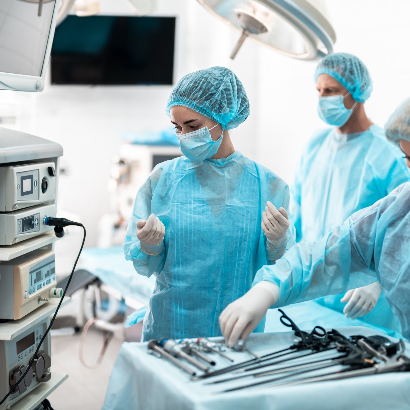 Nurses in protective masks and sterile gloves checking laparoscopic instruments and medical equipment