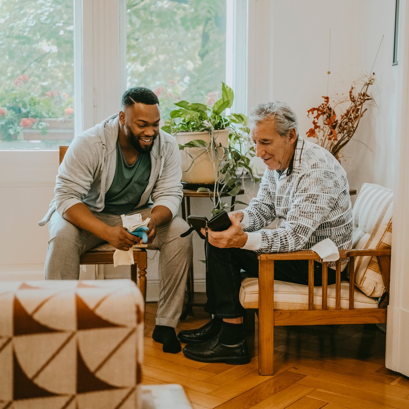Senior man sharing smart phone with male healthcare worker sitting in living room