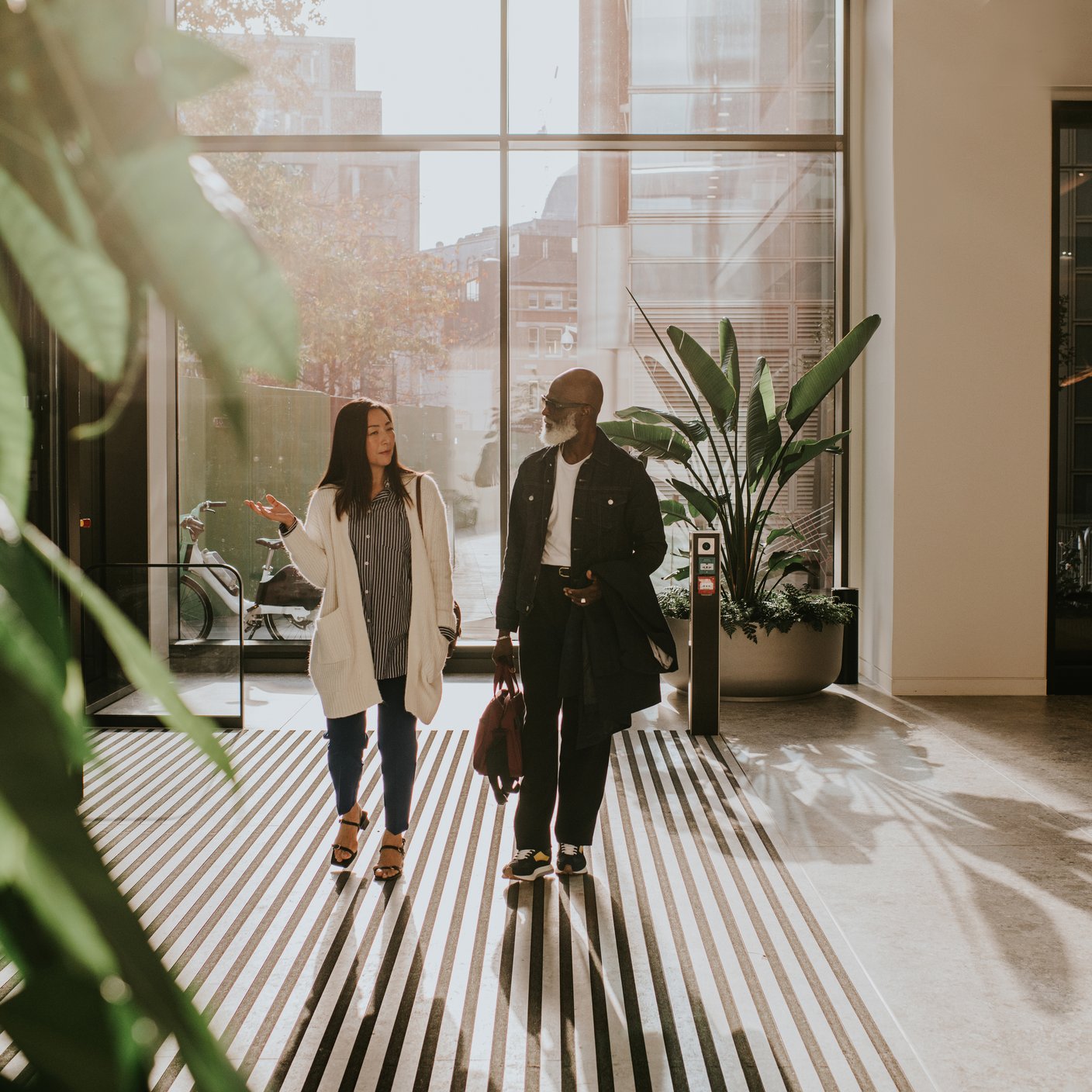 A man and woman enter a large, light filled interior space through rotating doors.