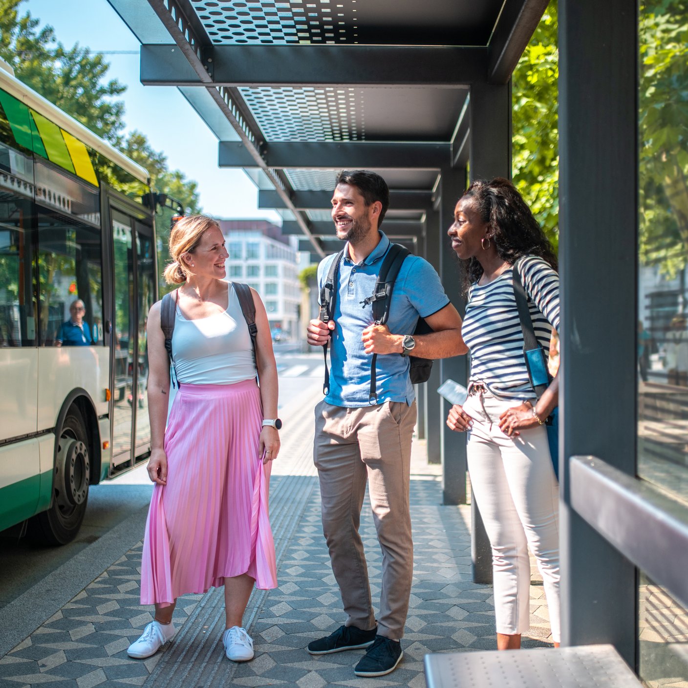 A group of diverse friends stand engaging in conversation at a sunny urban bus station