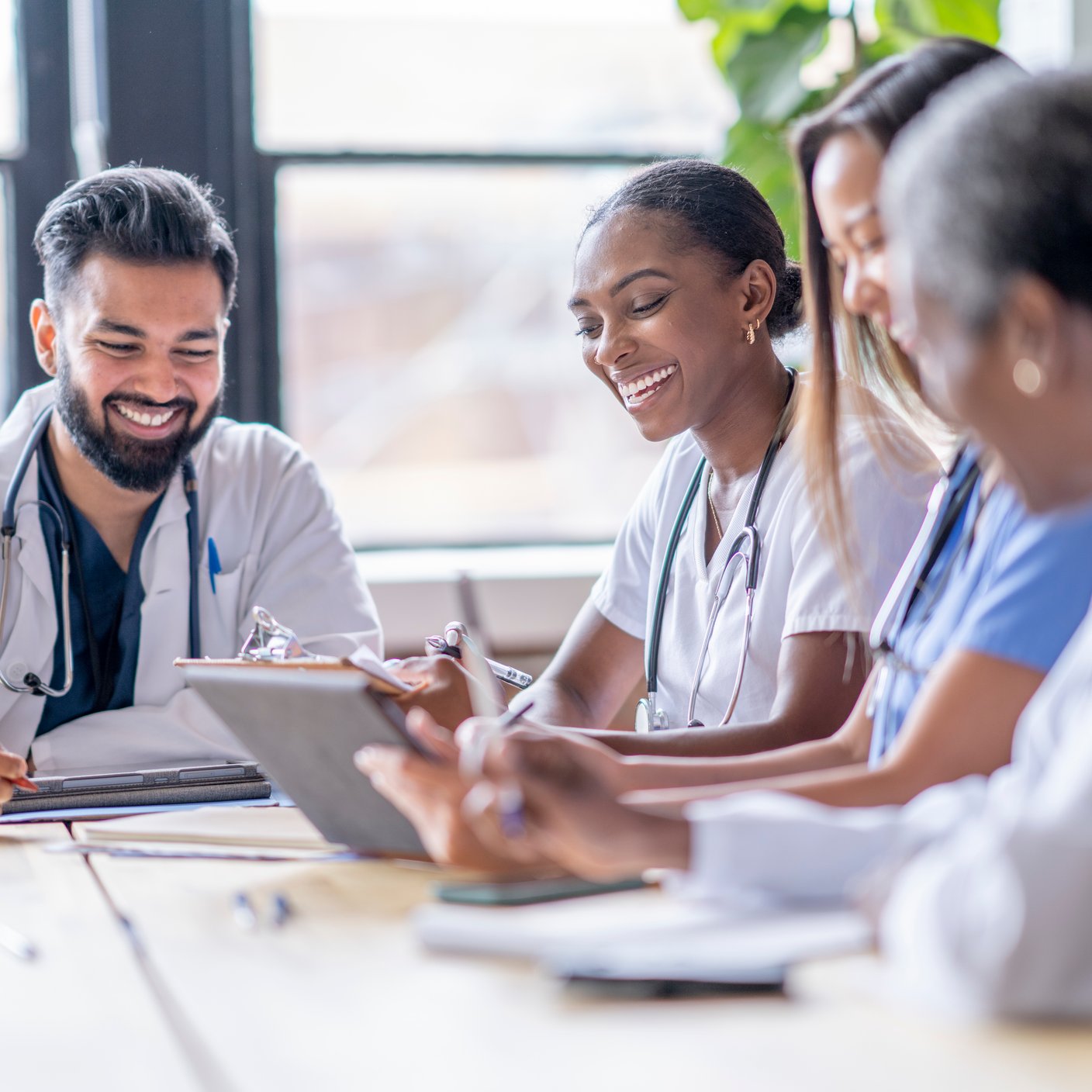 A small group of four medical professionals sit around a boardroom table as they meet to discuss patient cases.