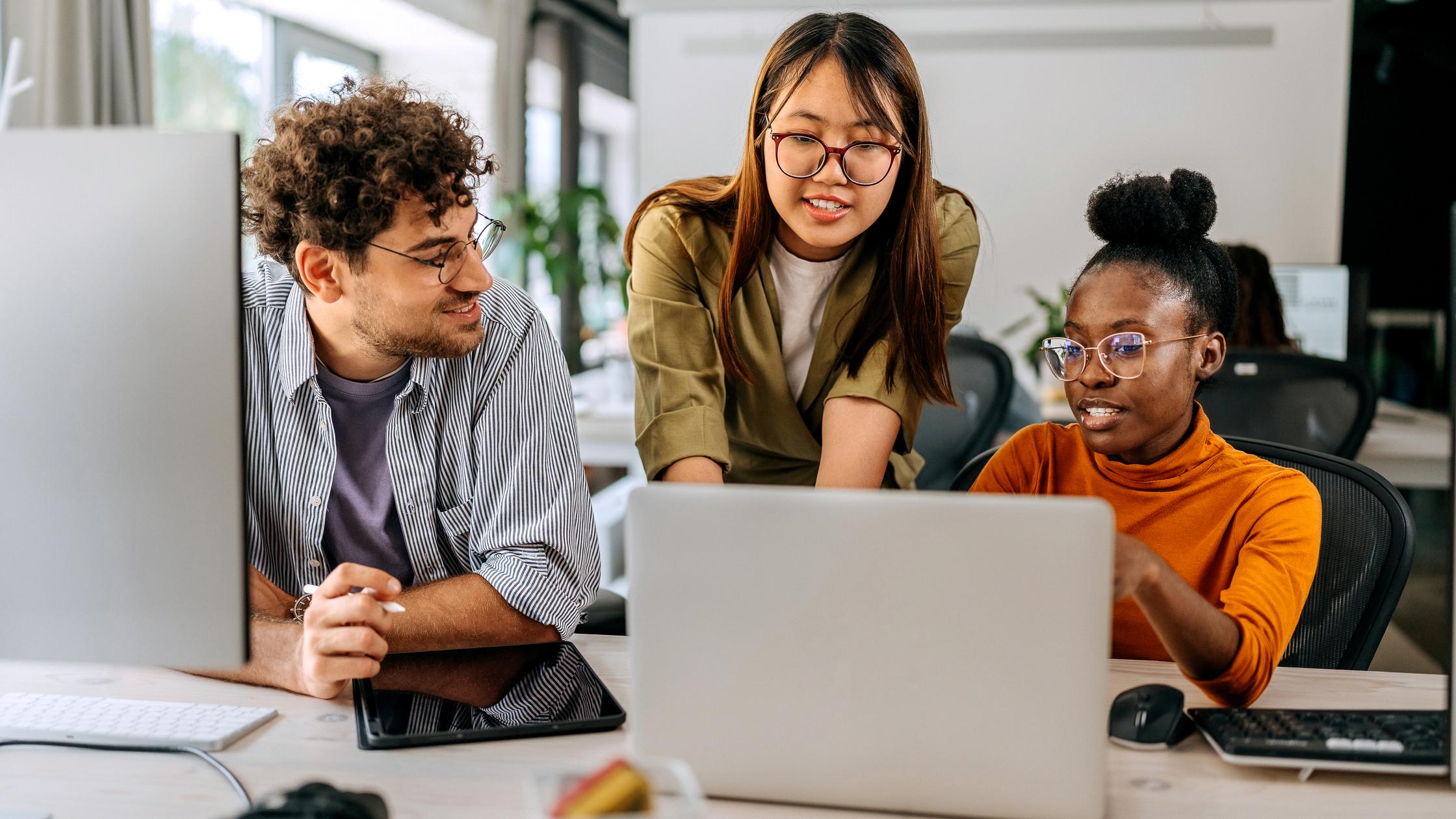 Drei Mitarbeiter versammeln sich um einen Laptop